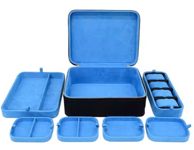 May include: A blue velvet lined watch box with a zipper closure. The box has multiple compartments for storing watches and other jewelry. The box is made of black hard plastic.