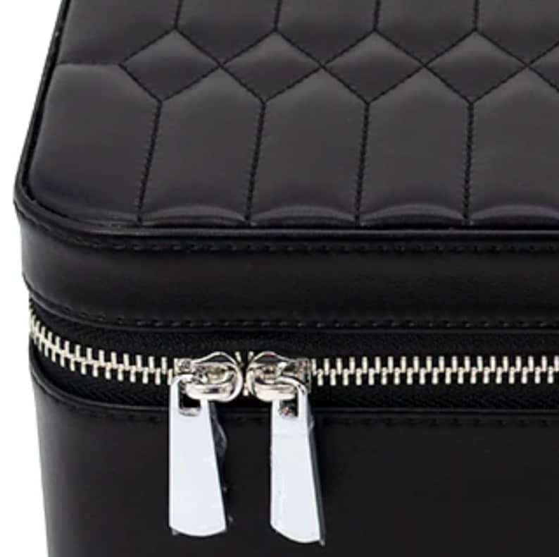 May include: Black quilted leather jewelry box with a silver zipper and two zipper pulls.