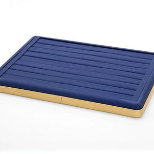 May include: A rectangular jewelry display tray with a navy blue, ridged top and a light brown wooden base. The tray is designed to hold rings and other small jewelry items. The tray is shown on a white background.