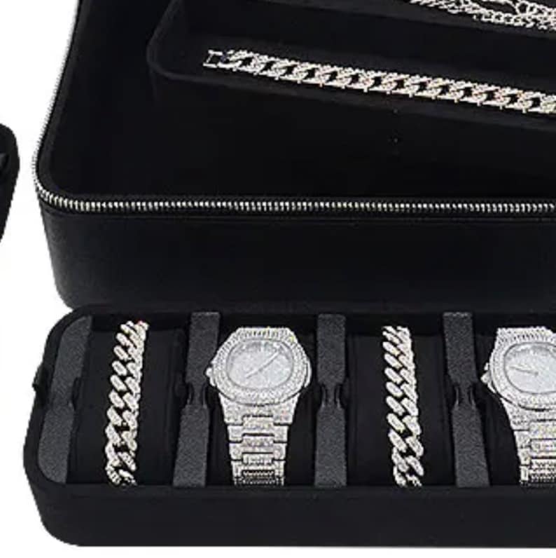 May include: Black leather case with multiple compartments for storing watches and jewelry. The case has a zipper closure and is lined with black velvet. The case is open and shows a variety of watches and chains with diamond accents.
