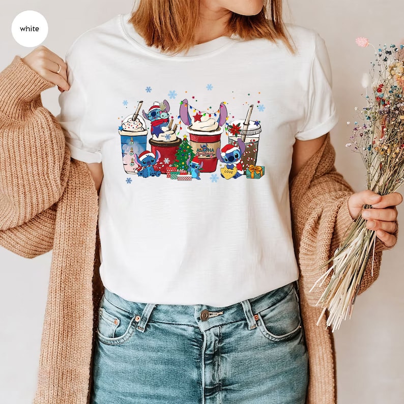 Peut inclure: T-shirt blanc avec un motif de No&euml;l repr&eacute;sentant Stitch de Lilo & Stitch. Le motif montre Stitch tenant une tasse de caf&eacute; avec un sapin de No&euml;l et des cadeaux. Le texte "Love" est sur la tasse.