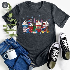 Peut inclure: Un t-shirt gris fonc&eacute; chin&eacute; avec un motif de No&euml;l repr&eacute;sentant des personnages de Stitch de Lilo & Stitch tenant des tasses de caf&eacute;. Le motif comprend un sapin de No&euml;l, des flocons de neige et les mots "Aloha" et "Love".