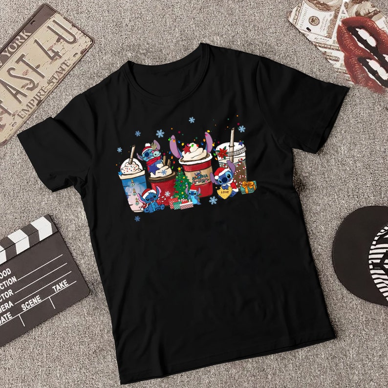 Peut inclure: T-shirt noir avec un motif de No&euml;l repr&eacute;sentant Stitch de Lilo & Stitch. Le motif montre Stitch tenant une tasse de caf&eacute; avec les mots "Aloha" et "Love" dessus. D'autres personnages de Stitch tiennent diff&eacute;rentes tasses de caf&eacute; et un petit sapin de No&euml;l.