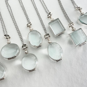 May include: Eight silver necklaces with different shaped glass locket pendants. The lockets are oval, square, and heart shaped. The necklaces are all on a white background.