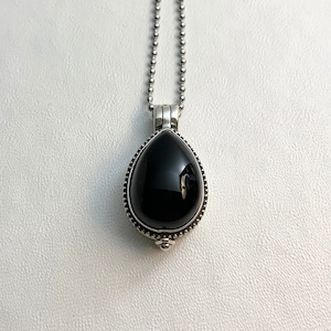 May include: A teardrop-shaped black onyx pendant necklace. The polished black stone is set in a silver-toned metal frame with a beaded border and hangs from a ball chain. The pendant is displayed against a white background.