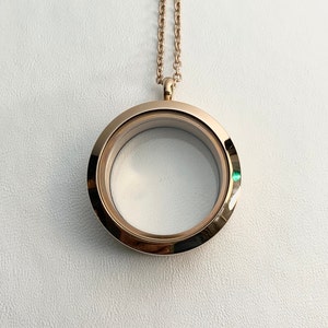 May include: A gold-toned locket necklace with a round, clear glass insert. The locket is open and ready to hold a photo or other small trinket.