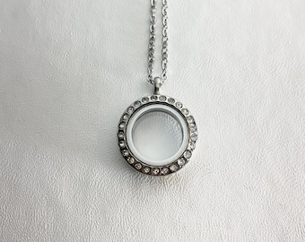 May include: A silver locket necklace with a clear glass insert and a circle of clear rhinestones around the edge.