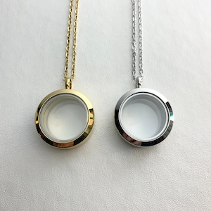 May include: Two locket necklaces, one gold and one silver, with a clear glass insert. The lockets are round and have a simple design.