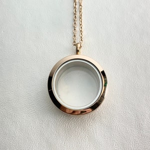 May include: A rose gold locket necklace with a clear glass insert. The locket is round and has a delicate chain.