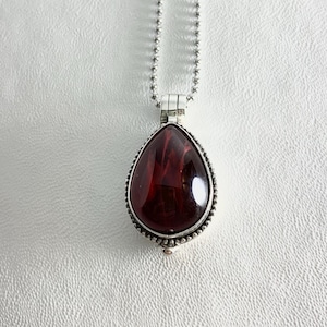 May include: A silver chain necklace with a teardrop-shaped pendant featuring a dark red gemstone.