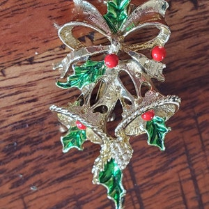 May include: Gold-tone Christmas bell brooch with a green holly leaf and red berry design. The brooch features a bow and two bells.