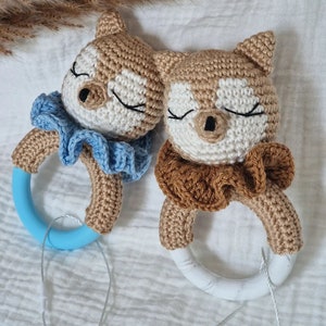 May include: Two crocheted fox rattle toys with blue and brown ruffled collars. The rattles have white marble rings.