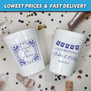 May include: Two white plastic cups with blue designs. One cup says "Viva Los Novios" with a decorative border. The other cup says "Celebrating Aiden & Kelly 06.02.2025" with a string of flags.