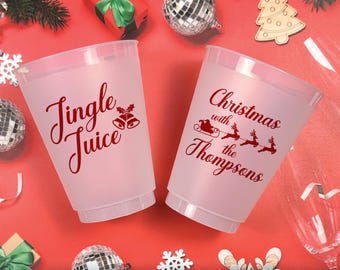 May include: Two frosted plastic cups featuring red holiday-themed text and graphics. One cup displays the text Jingle Juice with two bells. The other cup features the text Christmas with the Thompsons alongside a graphic of Santa in a sleigh.