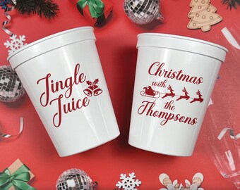 May include: Two white plastic stadium cups featuring red text and graphics. One cup displays the text Jingle Juice with a bell icon. The other cup displays the text Christmas with the Thompsons alongside a graphic of Santa in a sleigh with reindeer.