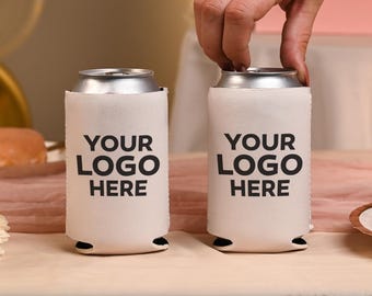 May include: Two white foam can coolers, each featuring the black text 'YOUR LOGO HERE' printed on the front. These cylindrical beverage insulators are designed to fit standard cans, providing a blank surface for custom branding and logos.