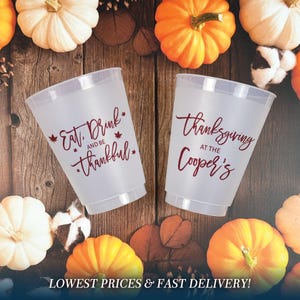 May include: Two frosted plastic cups featuring maroon text and maple leaf accents. The left cup displays the text Eat, Drink and be thankful, while the right cup features the text Thanksgiving AT THE Cooper's in a decorative script font.