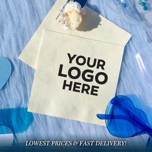 May include: A square, off-white paper napkin featuring the black text YOUR LOGO HERE printed in the centre. The napkin has a textured border and is positioned on a light blue fabric surface with a piece of cake and blue heart-shaped glasses.