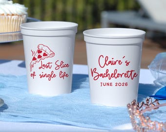 May include: Two white plastic stadium cups with red text and graphics. One cup features a pizza slice with heart-shaped pepperoni and the text "Last Slice of single life." The other cup displays the text "Claire's Bachelorette" and "JUNE 2026."