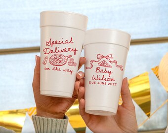 May include: Two white foam cups featuring red printed text and graphics. The left cup displays "Special Delivery on the way" with a baby bottle, pizza, and blocks. The right cup shows a bow, a pizza slice, and "Baby Wilson DUE JUNE 2027".
