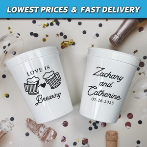 May include: Two white plastic cups with black text. One cup says "Love is Brewing" with a heart and two beer mugs. The other cup says "Zachary and Catherine 07.26.2025".