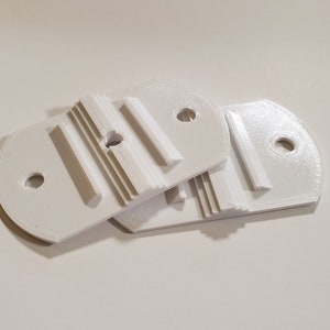 May include: Two white plastic brackets with a slot and a hole in each. The brackets are designed to be used for mounting.