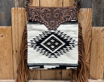 May include: A brown leather crossbody bag with a floral embossed design and a woven fabric panel featuring a black and white geometric pattern. The bag has long brown fringe and a shoulder strap.