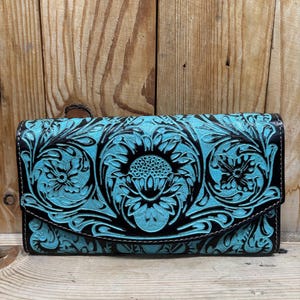 Peut inclure: Un portefeuille en cuir noir avec un motif floral turquoise. Le portefeuille a une fermeture à rabat et est décoré de motifs floraux complexes.