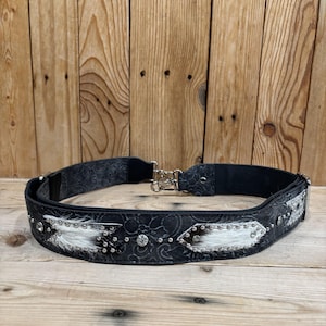 May include: Black belt with silver-tone buckle and decorative accents. The belt features a black patterned design with white fur and silver studs. Rhinestones are also incorporated into the design.