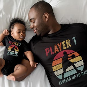 May include: Two people wearing black t-shirts with a retro design. The adult t-shirt says 