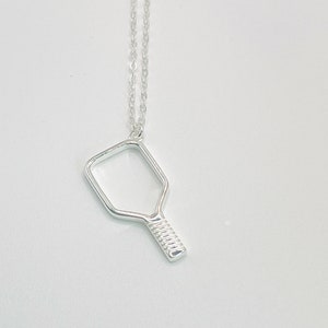 Peut inclure: Un collier en argent avec un pendentif en forme de raquette de pickleball.