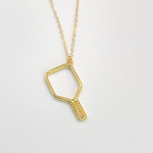 Peut inclure: Un collier en or avec un pendentif en forme de raquette de pickleball.