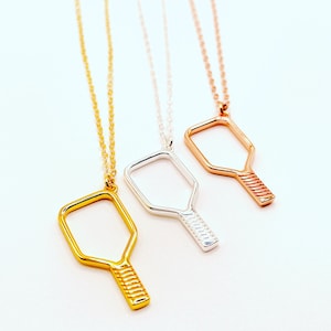 Peut inclure: Trois colliers en argent avec un pendentif en forme de raquette de pickleball. Les colliers sont en or, argent et or rose.