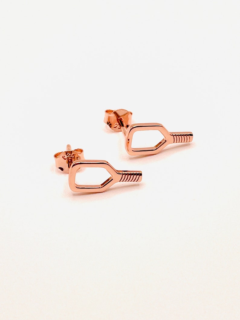 May include: A pair of rose gold earrings shaped like a paddle. The earrings are small and delicate.