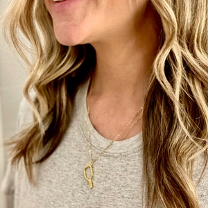 Peut inclure: Un collier en or avec un pendentif en forme de raquette, un &eacute;quipement de sport populaire. Le collier est port&eacute; par une personne aux cheveux longs et blonds.