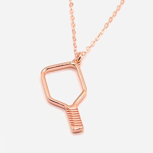 Peut inclure: Un collier en or rose avec un pendentif en forme de raquette de pickleball.