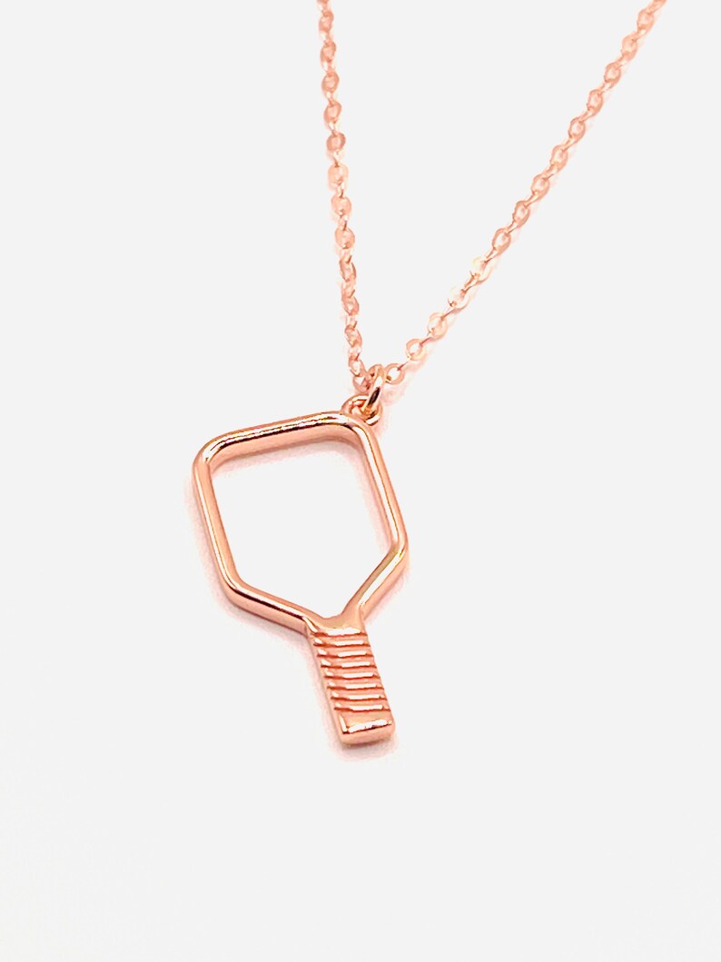 Peut inclure: Un collier en or rose avec un pendentif en forme de raquette de pickleball.