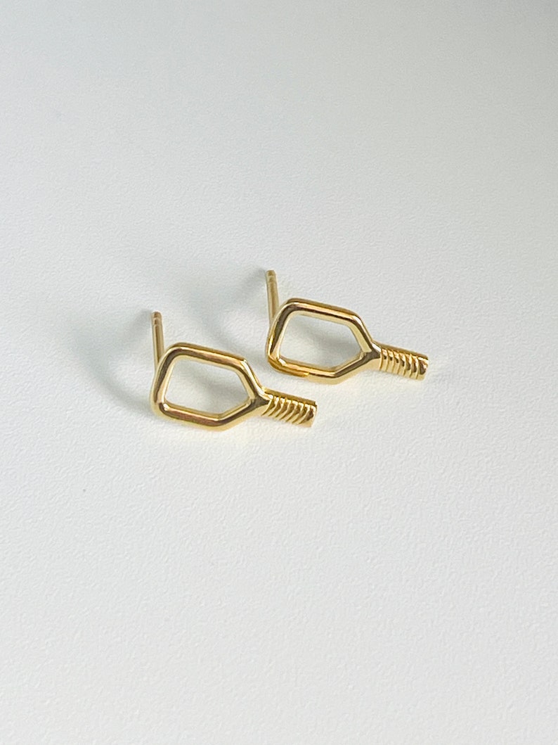May include: A pair of gold-toned earrings shaped like a paddle, a popular sport equipment used in the game of pickleball.