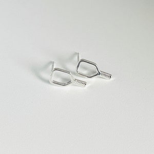 May include: A pair of silver earrings shaped like a pickleball paddle.