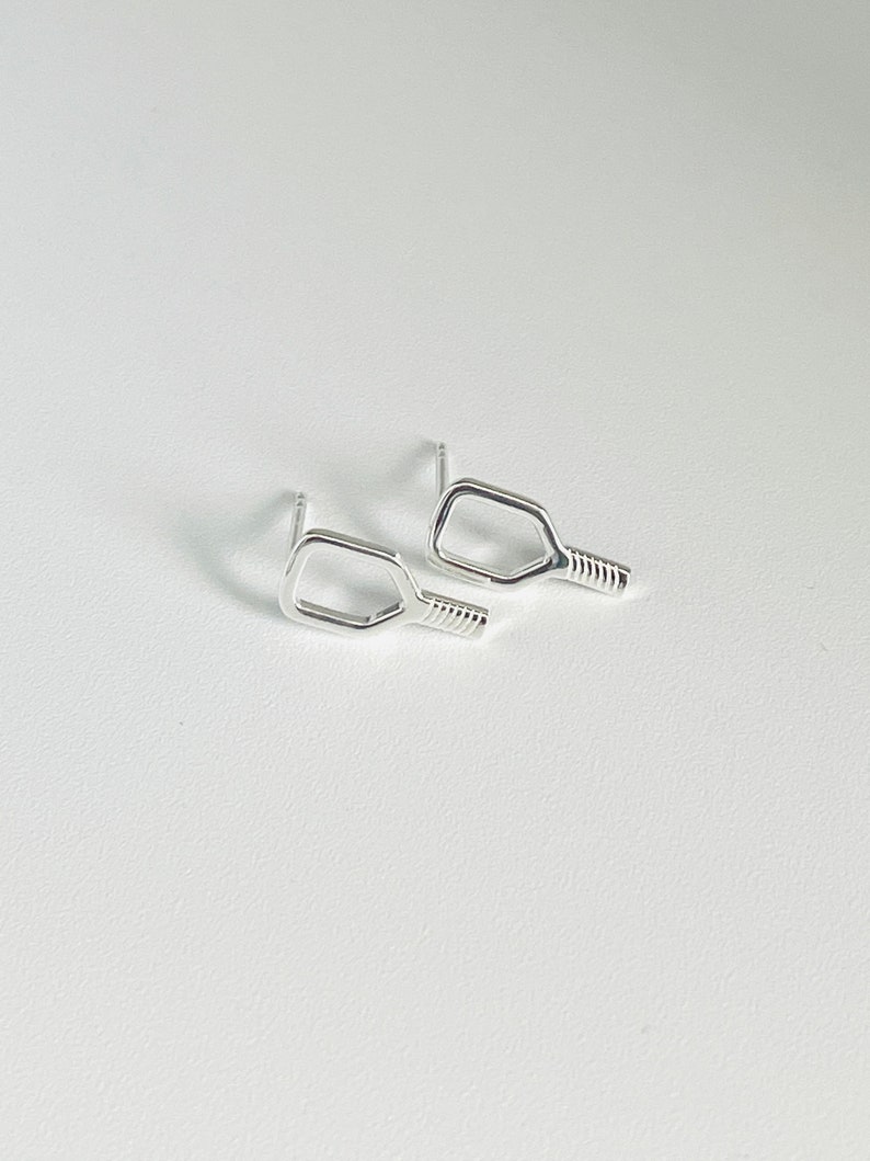 May include: A pair of silver earrings shaped like a pickleball paddle.