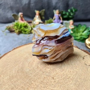 Puede incluir: Una gran pieza de vidrio de ópalo iridiscente, multicolor y en capas. El vidrio tiene una variedad de colores, incluyendo morado, blanco, marrón y azul. El vidrio está sentado sobre una superficie de madera.