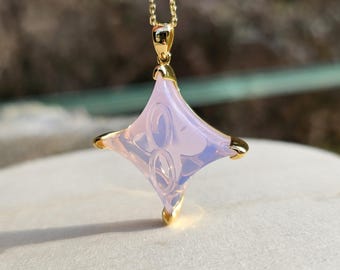 May include: A gold chain necklace with a pink, four-pointed star pendant. The star has a carved design and is translucent.