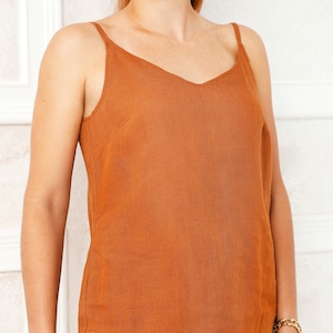 May include: A rust-colored linen tank top and matching shorts set. The top has a v-neck and thin straps. The shorts have a relaxed fit and a curved hem.
