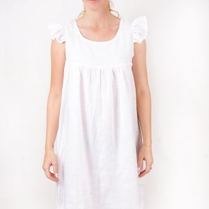 May include: A white linen dress with a scoop neck and short sleeves with ruffles. The dress has a gathered waist and a loose, flowing skirt.