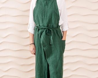 May include: A dark green linen apron with a wrap-around style and a large pocket. The apron has a wide belt that ties at the waist.
