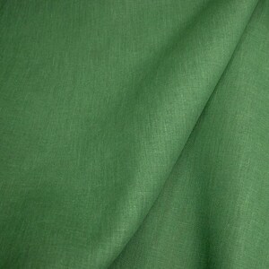 Op de afbeelding: Close-up van een gevouwen groene stof. De stof heeft een getextureerde uitstraling met zichtbare vezels en een lichte glans. De kleur is een levendig, medium groen, met subtiele kleurvariaties over het oppervlak.