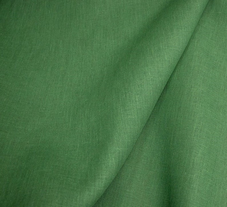Op de afbeelding: Close-up van een gevouwen groene stof. De stof heeft een getextureerde uitstraling met zichtbare vezels en een lichte glans. De kleur is een levendig, medium groen, met subtiele kleurvariaties over het oppervlak.