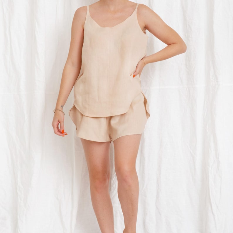 May include: A beige linen tank top and matching shorts set. The tank top has a scoop neck and thin straps. The shorts are a relaxed fit with a wide leg.