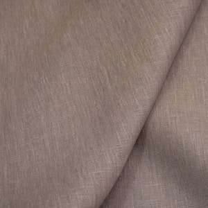 Op de afbeelding: Close-up van een gevouwen stuk taupekleurig linnen. De stof heeft een getextureerde uitstraling met zichtbare weefdetails. De plooien cre&euml;ren schaduwen, die de drapering en textuur van het materiaal benadrukken. De algehele esthetiek is eenvoudig en natuurlijk.