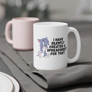 May include: White ceramic coffee mug with a cartoon cat and the text "I have silently created a spreadsheet for that".
